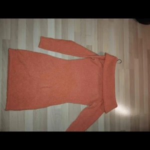 Orange stickad klänning - Säljer en mysig orange stickad klänning med lång ärm och polokrage. Perfekt för kyligare dagar och ger en härlig färgklick i garderoben. Klänningen har en tight passform som framhäver figuren.den här även ett litet hål längst ner men stans knappast, storlek s-m