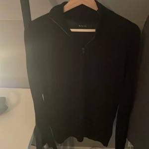 Svart merinoulltröja från Riley - Säljer en stilren svart tröja från Riley i mjuk merinoull. Tröjan har en dragkedja vid halsen och långa ärmar. Har använt en gång men o är i jättefint skick. 