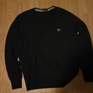 Svart tröja från GANT - Säljer en stilren svart tröja från GANT med broderad logga på bröstet. Tröjan har långa ärmar och en klassisk rund halsringning. Perfekt för en avslappnad men ändå snygg look.