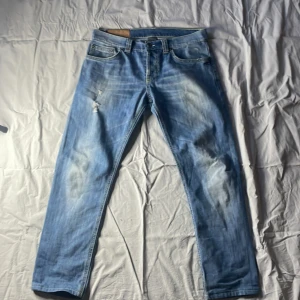 Ljusblåa dondups jeans  - Säljer ett par ljusblå jeansbyxor med slitna detaljer och klassisk femficksdesign. Byxorna har en knappgylf och är tillverkade i denim. Perfekta för en avslappnad stil.