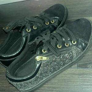 Svarta sneakers med glittriga detaljer - Snygga svarta sneakers med glittriga sidor och guldfärgade detaljer. Skorna har både snörning och dragkedja för en cool look. Perfekta för att ge din outfit lite extra bling skriv om du skulle vilja se dom på eller bara fler bilder på dom❤️