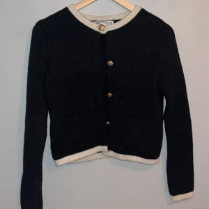 Svart kofta från Zara - Säljer en stilren svart kofta från Zara med vita detaljer vid krage, ärmslut och nederkant. Koftan har guldknappar framtill och två fickor. Perfekt för en elegant look💕.