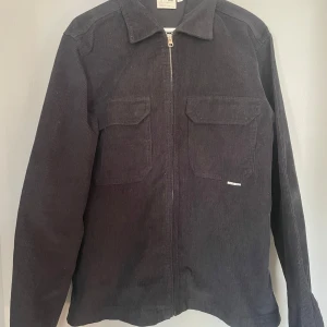 Svart manchesterjacka från Yôke - Säljer en stilren svart manchesterjacka från Yôke. Jackan har en dragkedja framtill och två bröstfickor med lock. Perfekt för en avslappnad och trendig look.