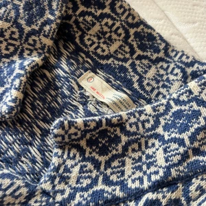 Blå och vit stickad kofta med broderad ros - Säljer en unik blå och vit stickad kofta från Rose and Blue. Den har ett vackert mönster och en broderad rosdetalj på ärmen. Koftan har långa ärmar och rosa rosetter på fickan. Perfekt för att hålla sig varm och stilren.