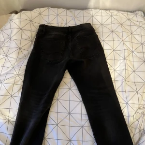 Svarta jeansbyxor - Snygga svarta jeansbyxor med en klassisk femficksdesign. De har en normal passform och är perfekta för en stilren look. Byxorna har en knapp och dragkedja framtill. 32/32