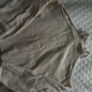 Beige långärmad tröja - Mysig beige tröja med lång ärm och öppna axlar, perfekt för kyligare dagar. Materialet är mjukt och bekvämt, vilket gör den idealisk för en avslappnad stil.