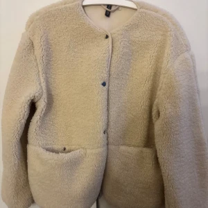Beige teddyjacka från H&M Divided - Mysig beige teddyjacka från H&M Divided med knappar framtill. Jackan har en rund halsringning och två  fickor. Använt max 5 gånger!!