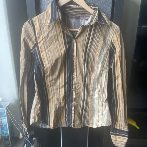Y2k skjorta från Jean Blanc - XS I PASSFORM!! Säljer en stilren randig skjorta från Jean Blanc i beige, svart och blå. Skjortan har långa ärmar och knappar framtill.