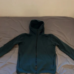 Mörkgrön hoodie från Peak Performance - Säljer en snygg mörkgrön hoodie från Peak Performance. Den har en dragkedja framtill och en bekväm huva. Perfekt för kyliga dagar eller som ett extra lager.