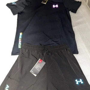 Svart set  från Under Armour - Under Armour Herr Sportset – T-shirt & Shorts (Ny med taggar) Storlek: M/S Färg: Svart med reflekterande logotyper  Fin, torr och stilig under träningspasset eller till vardags med detta helt nya sportset från Under Armour. Setet består av en funktionell t-shirt och ett par lätta shorts, båda designade för komfort, andningsförmåga och rörelsefrihet.