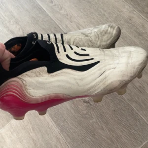 Fotbollsskor Adidas copa  - Säljer ett par vita fotbollsskor med rosa detaljer och svarta inslag. Skorna är rätt smutsiga o har spruckit lite här o där men fortfarande goa o spela i.