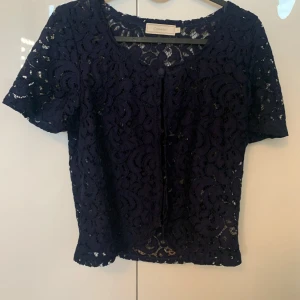 Mörkblå spetsblus från Cream - Säljer en elegant mörkblå spetsblus från Cream. Blusen har korta ärmar och knappar framtill. Perfekt för att ge en stilfull touch till din outfit.