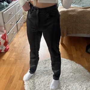 Svarta skinnbyxor - Snygga svarta skinnbyxor med hög midja. Byxorna har en rak passform och är perfekta för en stilren look. De är tillverkade i ett glansigt material som ger en cool och modern känsla.