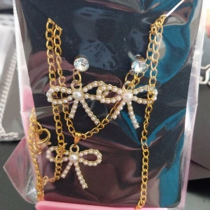 Guldpläterat smyckeset med pärlor och rosetter - Säljer ett smyckeset med guldpläterad kedja, örhängen med glittrande stenar och matchande halsband och armband med vita pärlor formade som rosetter. Perfekt för dig som gillar söta detaljer och elegant stil. Egen tillverkning.. 150 kr per sett