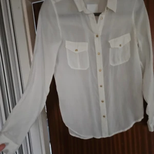 Vit blus från InWear med guldknappar - Säljer en stilren vit blus från InWear i storlek S. Blusen har lång ärm, två bröstfickor och snygga guldiga knappar framtill. Tunt och lätt material som ger en luftig känsla. Perfekt för dig som gillar klassisk och enkel stil.