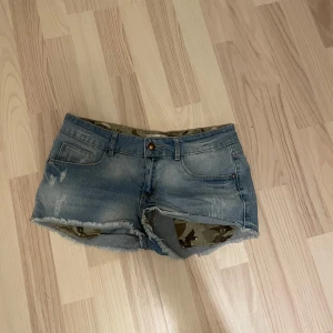 Blå lowwaist jeansshorts med camo-detaljer från Denim Life - Säljer ett par blå lowwasit jeansshorts från Denim Life med slitna detaljer och fransig kant. Insidan har ett camouflagemönster som också syns vid fickorna. Perfekta för sommaren. Står ingen strl och köpte för längesen som tyvärr inte passar. Skulle säga att det är typ strl S. Pris är diskuterbart