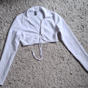 Vit croppad långärmad topp med knyt - Säljer en vit croppad topp med lång ärm och krage. Toppen har knytning framtill och en snygg v-ringning. Skriv innan ni köper!