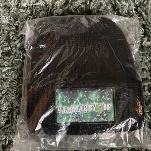 Svart stickad mössa med Hammarby IF-märke - Svart stickad mössa med stort broderat Hammarby IF-märke framtill. Perfekt för dig som vill visa ditt stöd för laget och hålla dig varm under kalla dagar.