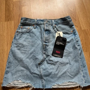 Ljusblå jeanskjol från Levi's - Levis High-Rise deconstructed kjol säljer pgr av att den är för stor för mig, köptes för ca 2,5 år sen på zalando om jag minns rätt, med ett hopp om att jag skulle växa i den, vilket jag inte gjort och sen glömt av att den funnits i garderoben. Aldrig använd, endast testad, lappar sitter kvar, strl 26, nypris 600kr. Köpare står för ev frakt