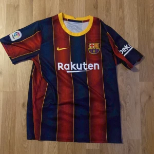 FC Barcelona hemmatröja Nike - Säljer en FC Barcelona hemmatröja från Nike med Rakuten som sponsor. Tröjan är randig i blått och rött med gula detaljer och klubbmärke på bröstet. La Liga-märke på ärmen och Beko-logga på andra ärmen. Perfekt för dig som älskar Barca!