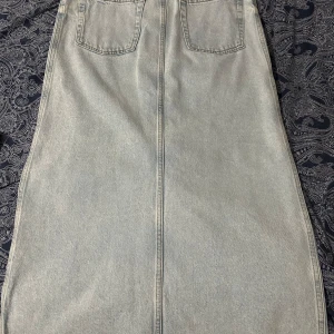Ljusblå jeanskjol med slits - Säljer en ljusblå jeanskjol med två bakfickor och en snygg slits bak. Kjolen har klassisk jeanssöm och dragkedja framtill. Perfekt för dig som gillar enkel och stilren denim.
