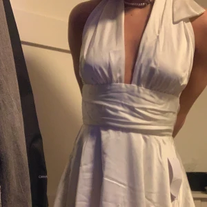 Vit studentklänning från bubbleroom - Säljer en vit kortklänning från Bubbleroom med halterneck och öppen rygg. Klänningen har omlottknytning i midjan och en elegant, figurnära passform upptill. Perfekt för student. Lappen finns kvar, den är helt oanvänd. 