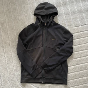 Svart hoodie från BOSS - Säljer en svart hoodie från Hugo BOSS med dragkedja framtill och huva i väldigt bra skick!🦋 • Storlek L • Frakt tillkommer  • Har du några frågor är det bara att skicka ett meddelande, så svarar jag så fort jag kan.☺️ Ha en fin dag!💕♻️
