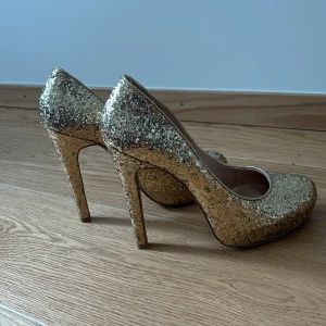 Glittriga  hög klackar  - Säljer ett par  guld glittriga hög klackar. Okej skick. Har för det mesta stått i garderoben.