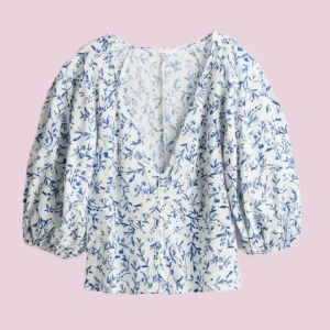 Vit blus med blått blommönster och puffärmar - Säljer en vit blus med blått blommönster och stora puffärmar. Blusen har v-ringning, knappar framtill och är tillverkad i ett lätt bomullstyg. Perfekt för vår och sommar!