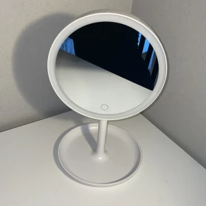 Vit sminkspegel med LED-belysning - Rund sminkspegel i vit plast med inbyggd LED-belysning och touchknapp på framsidan. Baksidan har en mindre förstoringsspegel. Perfekt för sminkrutinen och enkel att placera på sminkbordet. Obs! Batteri till lampan kommer inte med