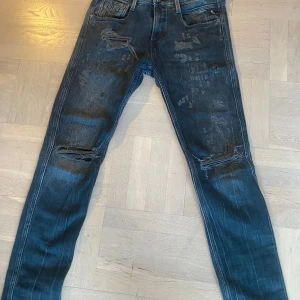 Replay Anbass jeans med slitningar - Säljer ett par mörkblå Replay Anbass jeans med snygga slitningar och detaljerade revor på benen. Modellen är slim fit och har klassisk femficksdesign. Perfekta för dig som gillar en trendig och avslappnad stil.