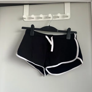 Svarta shorts - Svarta shorts från F2 Sister med vit kant och snörning i midjan. Sportig modell med korta ben och rundade sidor. Perfekta för träning eller avslappnade dagar.