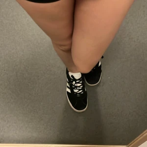 Svarta Adidas sneakers  - Säljer ett par klassiska svarta Adidas sneakers med vita ränder på sidorna och vit sula. Skorna har snörning och en sportig, tidlös design som passar till många olika outfits.