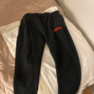 Svarta mjukisbyxor från Hoodrich - Svarta mjukisbyxor från Hoodrich med röd logga tryckt på vänster lår. Byxorna har dragsko i midjan och sidofickor. Perfekta för en avslappnad stil och riktigt sköna att ha på sig.