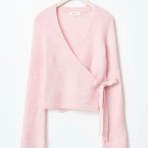 Rosa omlottkofta - Superfin ljusrosa omlottkofta med knyt i sidan. Tröjan har lång ärm och är stickad i ett mjukt material. Perfekt för lager-på-lager och ger en söt touch till din outfit. Slup på hemsidan och endast använd 2 gånger!!💕storlek M men sitter som en S