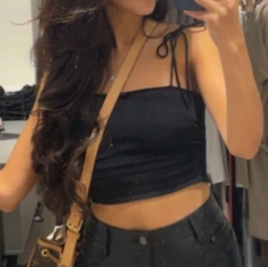 Svart croppad tubtopp med knytband - Säljer en svart croppad tubtopp med smala axelband som knyts på axlarna. Toppen är enkel och stilren, perfekt till sommaren och att matcha med höga byxor eller kjol.