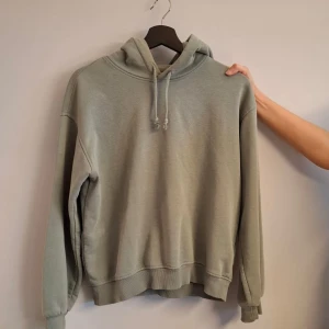Grön hoodie med luva - Säljer en enkel och stilren grön hoodie med luva. Tröjan har långa ärmar och en avslappnad passform.