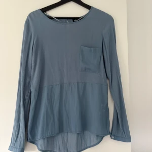 Ljusblå långärmad blus från KappAhl - Säljer en ljusblå blus från KappAhl i storlek 34. Blusen har lång ärm, rund halsringning och en bröstficka. Materialet är tunt och lätt, perfekt för lager-på-lager. Baksidan har en liten knappdetalj vid nacken.