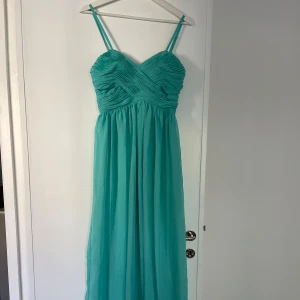Turkos långklänning med smala axelband - Säljer en grön långklänning med smala axelband och v-ringad överdel. Klänningen har draperad byst och ett luftigt, fallande tyg som ger en elegant känsla. Perfekt för sommarens speciella tillfällen!