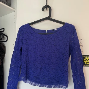 Blå spetsblus med dragkedja - Säljer en blå långärmad blus i spets med rund halsringning och dragkedja bak. Blusen är croppad och har fina blommiga spetsdetaljer. Perfekt för dig som vill ha något snyggt och unikt i garderoben!