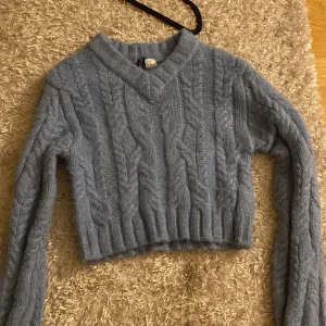 Ljusblå stickad croppad tröja från H&M Divided - Supermjuk ljusblå stickad tröja från H&M Divided. Tröjan är croppad med kabelstickat mönster och har långa ärmar samt v-ringad hals. Perfekt för lager-på-lager och chill dagar.