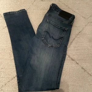Blå slim fit jeans från Jack & Jones - Snygga blå jeans från Jack & Jones i modellen SLIM/GLENN. Jeansen har klassisk femficksdesign, knappgylf och diskreta slitningar för en modern look. Perfekta för dig som gillar en smal passform och stilren denim. Hör av dig vid minsta lilla fundering.