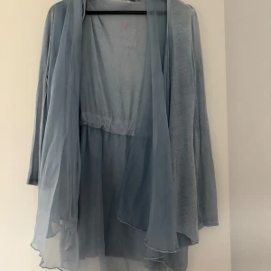 Ljusblå cardigan kofta från Svinth's Bible - Säljer en ljusblå, tunn och flowy cardigan kofta från Svinth's Bible by Aqenurm. Koftan har lång ärm och öppen front med lätt, transparent tyg som ger en luftig känsla. Perfekt för lager-på-lager och tillverkad i Italien. Vet ej storlek men mellan S-M