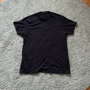 Svart t-shirt från Tommy Hilfiger - Säljer en klassisk svart t-shirt från Tommy Hilfiger med liten logga på bröstet. T-shirten har rund halsringning och korta ärmar. Perfekt och skön till sommaren. Har inte använts nånting och är sprillans ny. Storlek S men passar även M. Hör av dig vid fundering. MVH Holger!👍👍