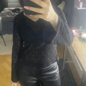 Svart spetsig långärmad topp - Säljer en svart långärmad topp med spetsdetaljer och v-ringning. Toppens material är genombrutet och ger en elegant look. Perfekt att styla med både jeans och kjol.