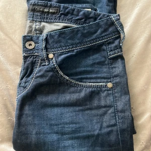 Blå bootcut jeans från Calvin Klein - Säljer ett par mörkblå bootcut jeans från Calvin Klein med kontrastsömmar och klassiska fickor. Jeansen har en snygg utsvängd passform och tydlig logga på bakfickan. Perfekta för dig som gillar retrostil.