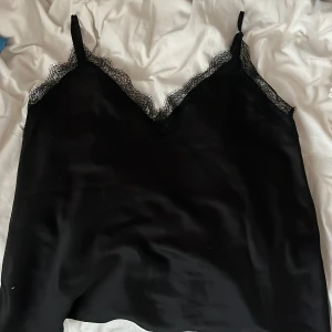 Svart linnetopp med spetsdetaljer - Säljer en svart linnetopp med tunna axelband och v-ringning. Från början är det tänk att det ska vara ett pyjamaslinne men jag har använt det några enstaka gånger bara som ett vanligt linne, vilket som fungerar bra!💕