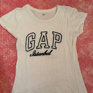 Vit GAP t-shirt  - Vit t-shirt från GAP med broderad svart text 'GAP Istanbul' på bröstet. Klassisk rund hals och korta ärmar. T-shirten är i mjuk bomull och har en clean, sportig vibe som passar perfekt till jeans eller shorts. Passar som S 