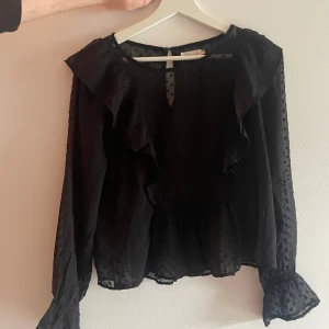 Svart prickig blus  - Supersöt svart blus från lager 157 med transparenta ärmar, volangdetaljer och prickigt mönster. Lätt och luftig med lång ärm och knäppning bak i nacken. Perfekt när du vill ha något extra till din outfit. Strl s. Går bra att pruta. Använd 2 gånger 