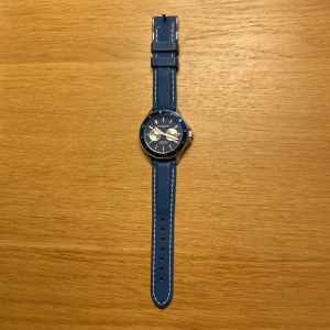 Blå Philippe Palmer klocka - Snygg klocka från Philippe Palmer med blått armband och blå urtavla. Klockan har silverfärgade detaljer, två mindre urtavlor och tydliga siffror på ringen. Armbandet är i syntetmaterial med vita sömmar. Vattentät till 30 meter och har japanskt kvartsverk. Knappt använd 